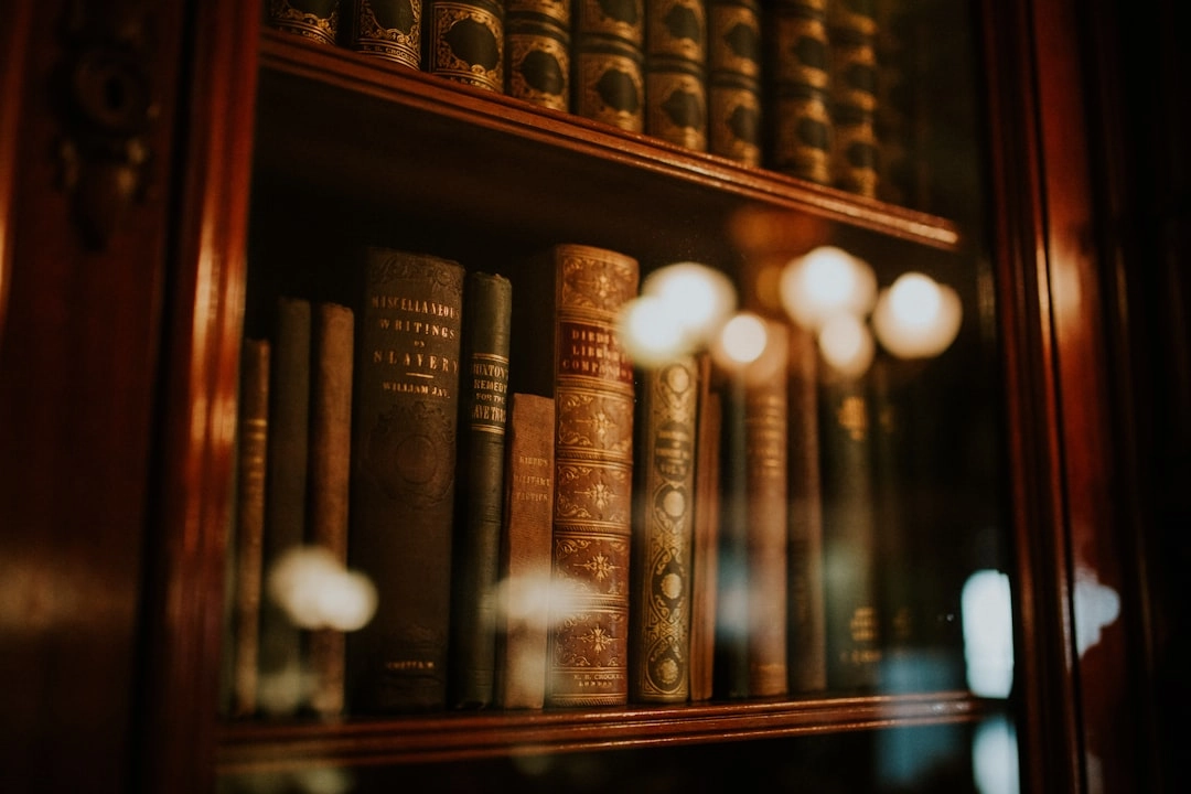 Antique leather-bound books on wooden shelves behind glass, with warm light reflections on the case.