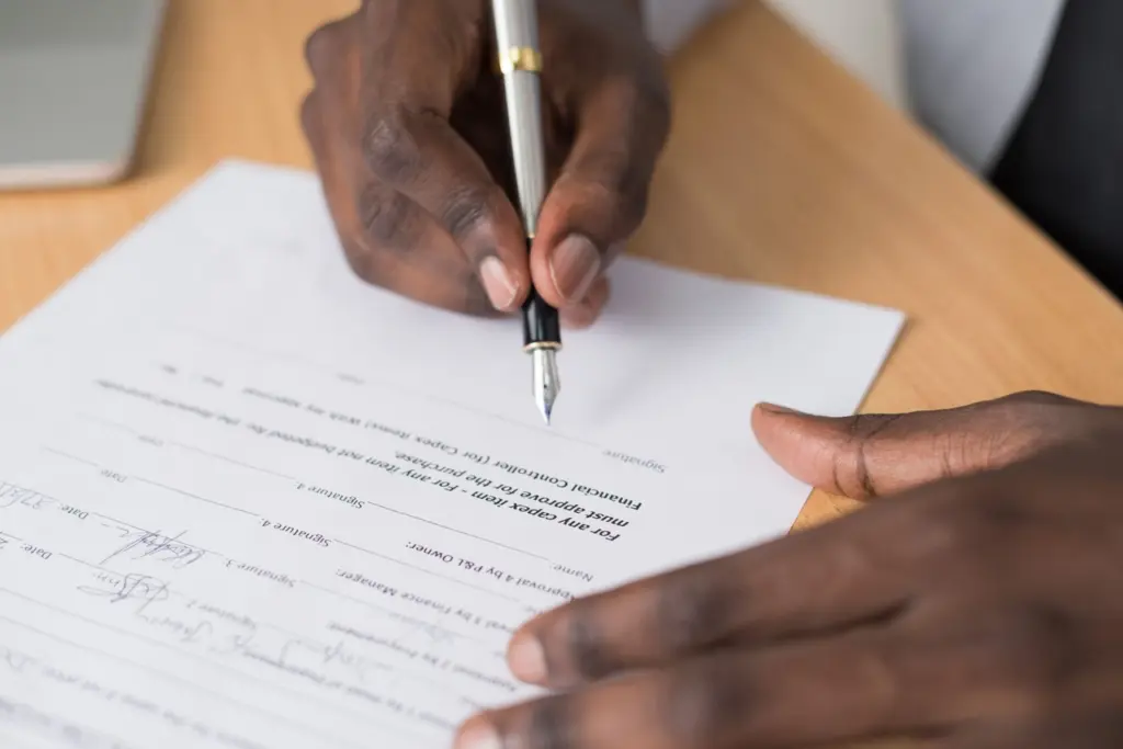 Close-up of hands signing a contract document with a fountain pen on a wooden desk