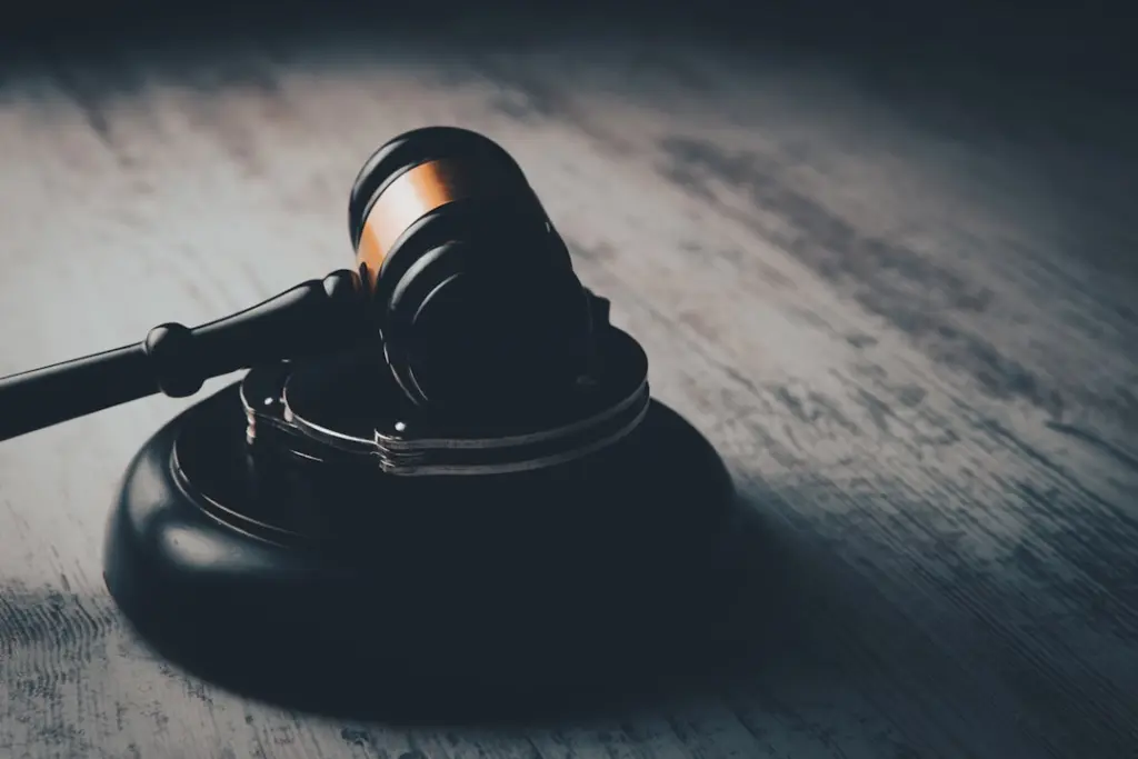 Black wooden gavel resting on a sound block with metal handcuffs draped over it on a weathered wood surface