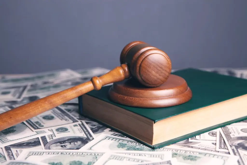 Wooden gavel resting on a green law book surrounded by scattered hundred dollar bills