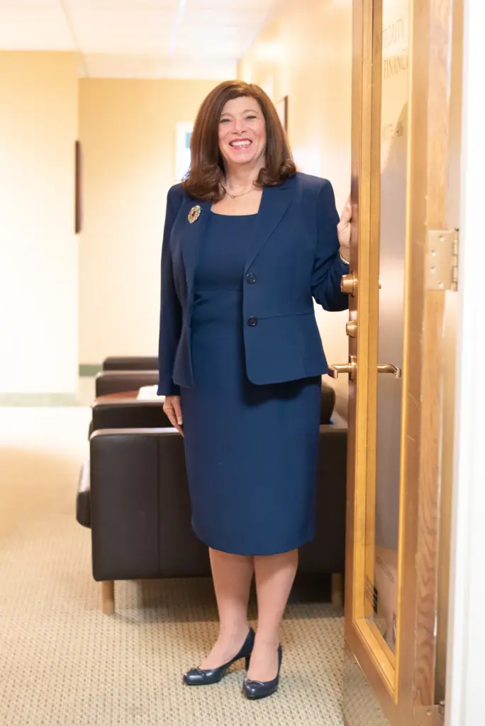 Smiling woman in a navy suit standing at the open office door of Integrity Finance, with a waiting area behind her.
