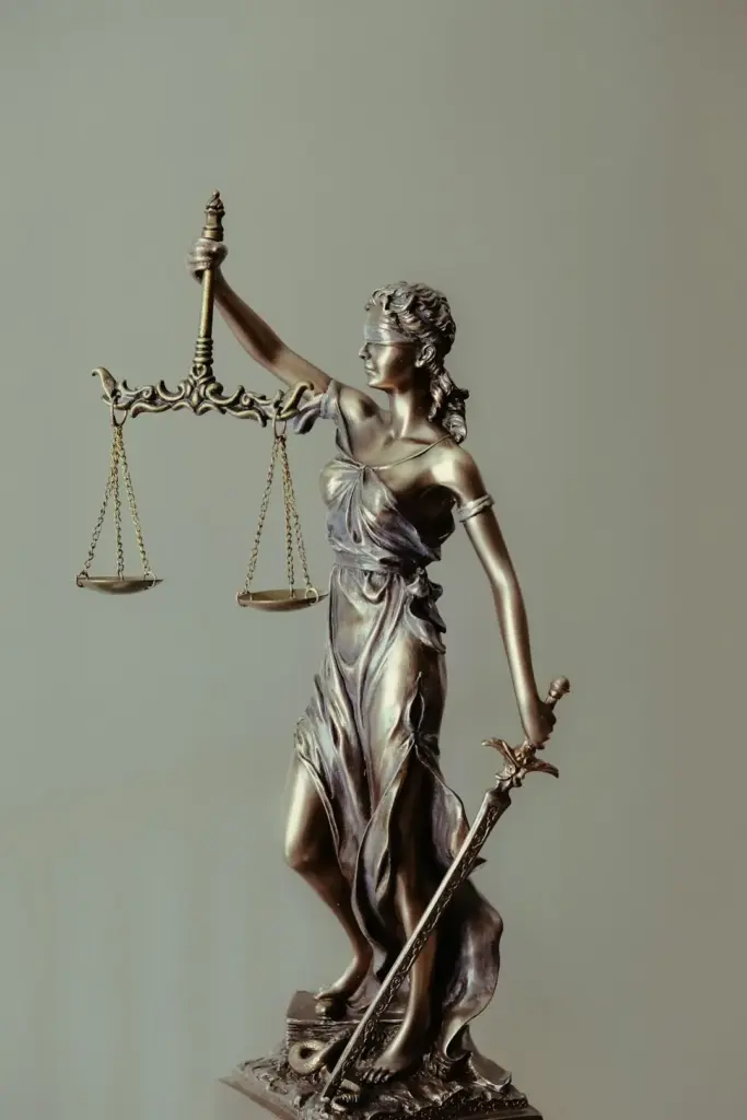 Bronze Lady Justice statue holding scales and a sword, blindfolded, against a plain gray background.