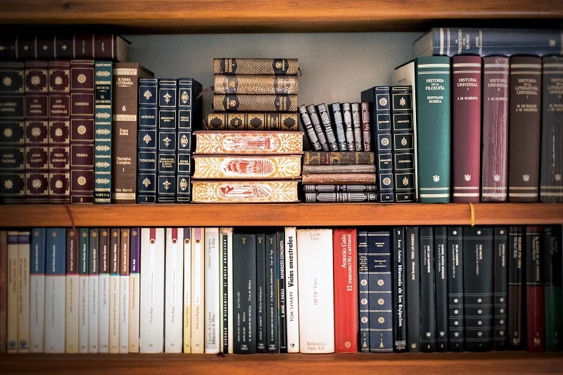 Two wooden bookshelves filled with leather-bound classics, Spanish-language literature, and stacked antique volumes.