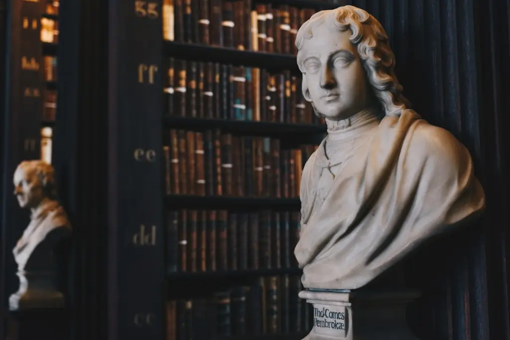 White marble bust of a figure in classical dress in front of dark shelves filled with antique leather-bound books.